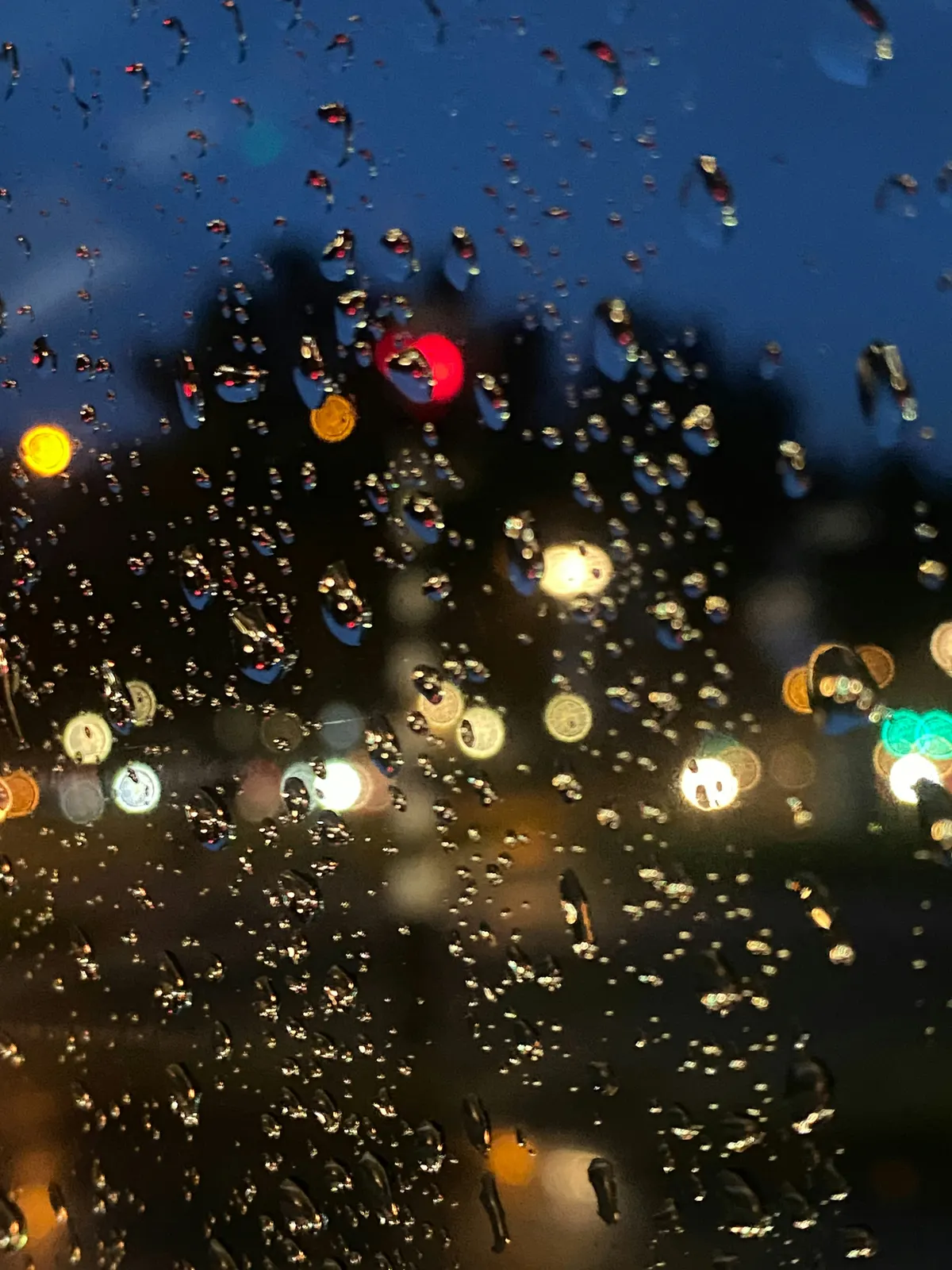 Rain on a car window at night, with blurred street lights